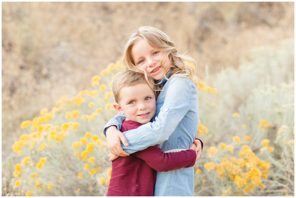 Brother and sister hugging each other in front of yellow flowers Family Pictures at Anderson Dam Miranda Renee Photography