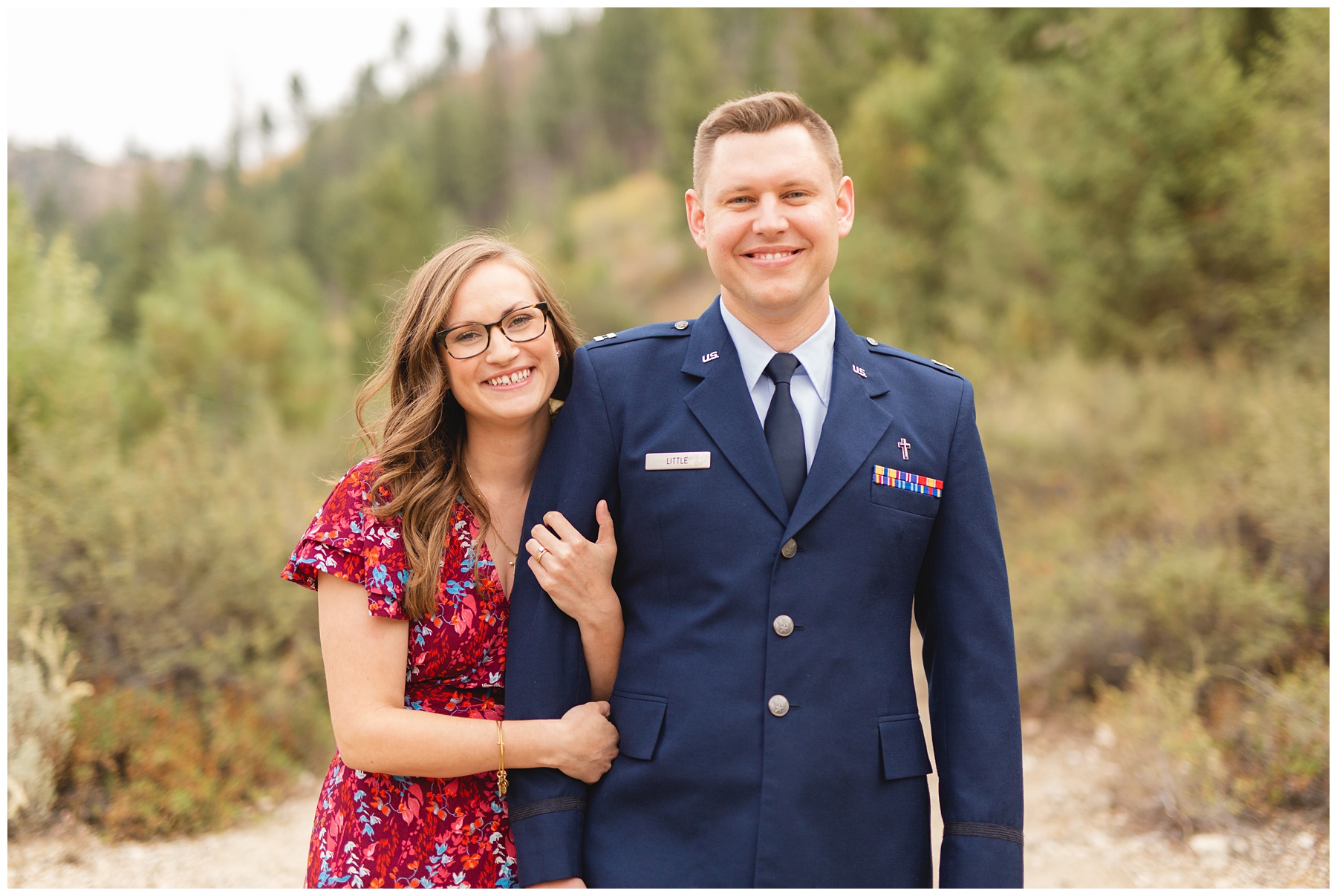man in united states air force blues looking at camera smiling with wife on his arm. Photo by Miranda Renee Photography