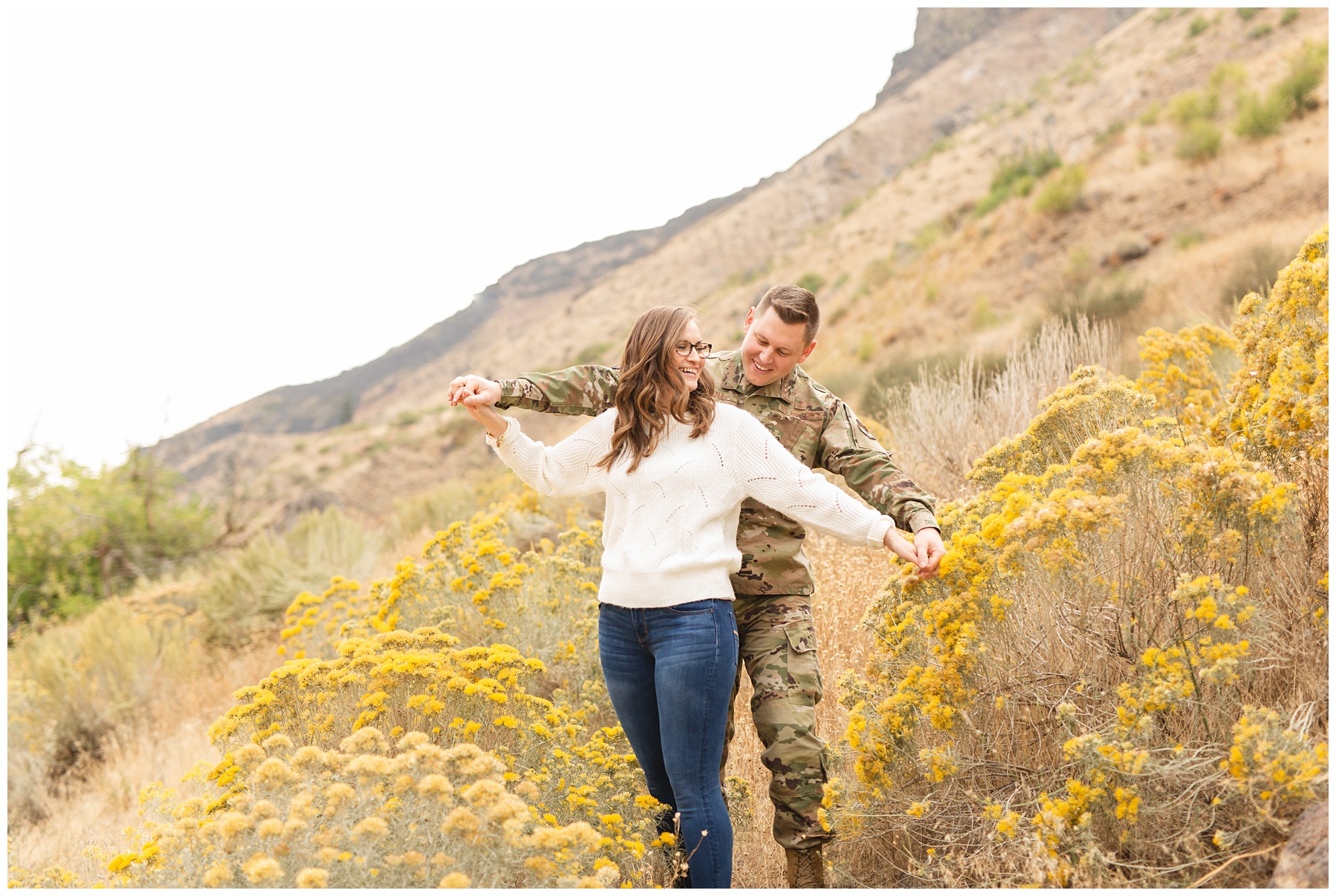 couple pretending to be an airplane in Boise Idaho for their photo session. man in military camo surrounded by mustard bushes