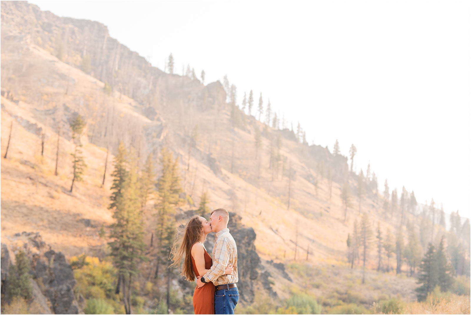 Couple kissing during couples' photo session with mountain cliffs in the background in Boise Idaho. Photo by Miranda Renee Photography