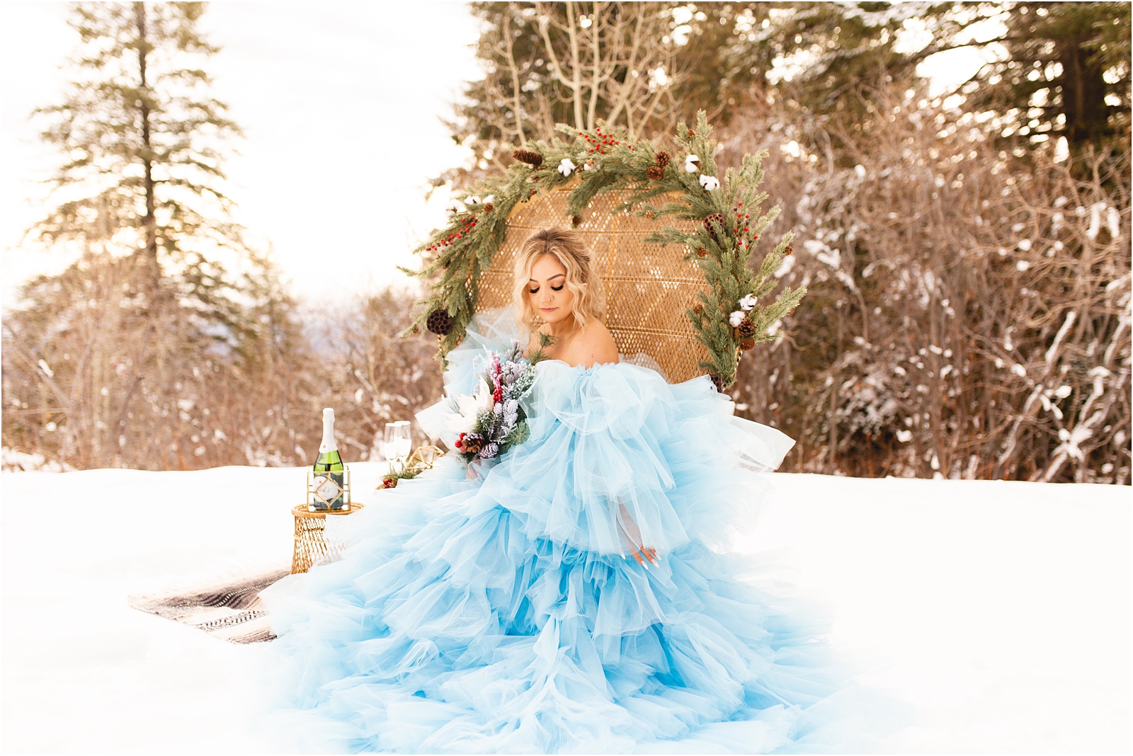 Winter Wedding in Idaho. bride sitting in peacock chair on a snowy mountain in a blue chiffon dress