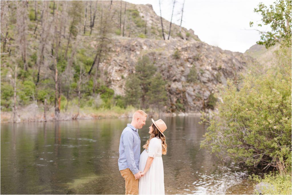 Couple facing each other and holding hands by the Boise River at Anderson Dam