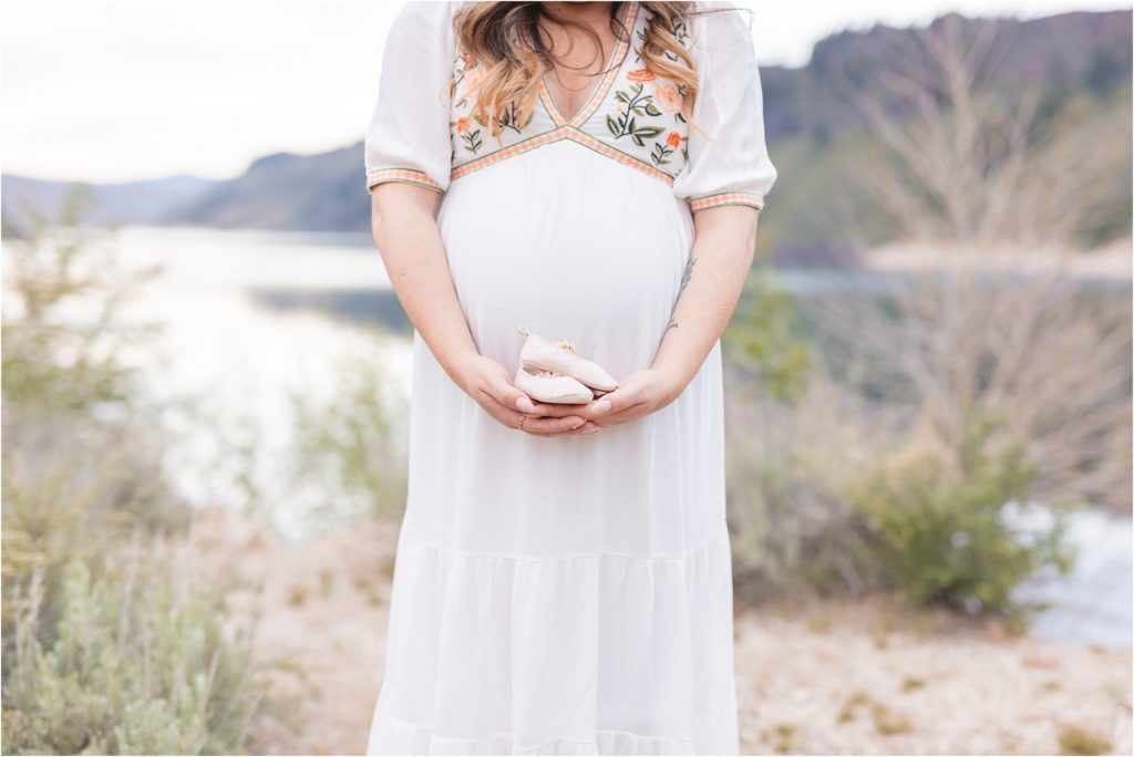 Pregnant mom holding baby girl shoes in front of her pregnant belly in Boise Idaho
