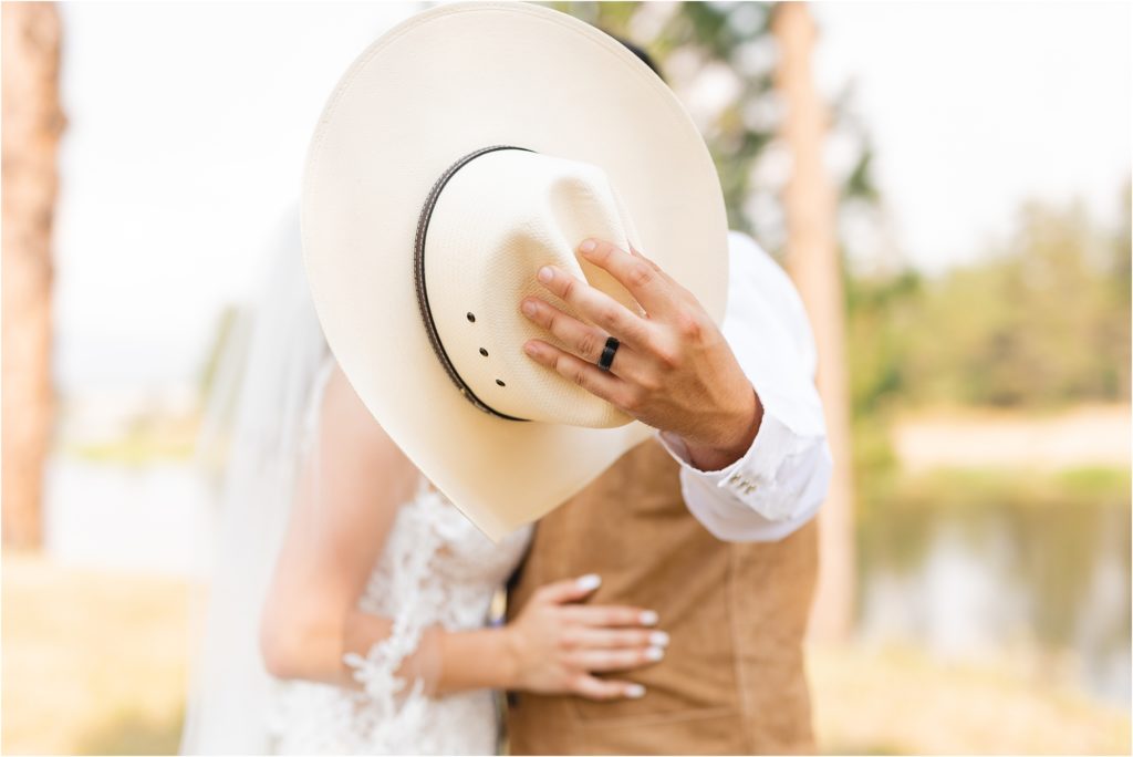 groom holding cowboy hat to cover kiss with bride