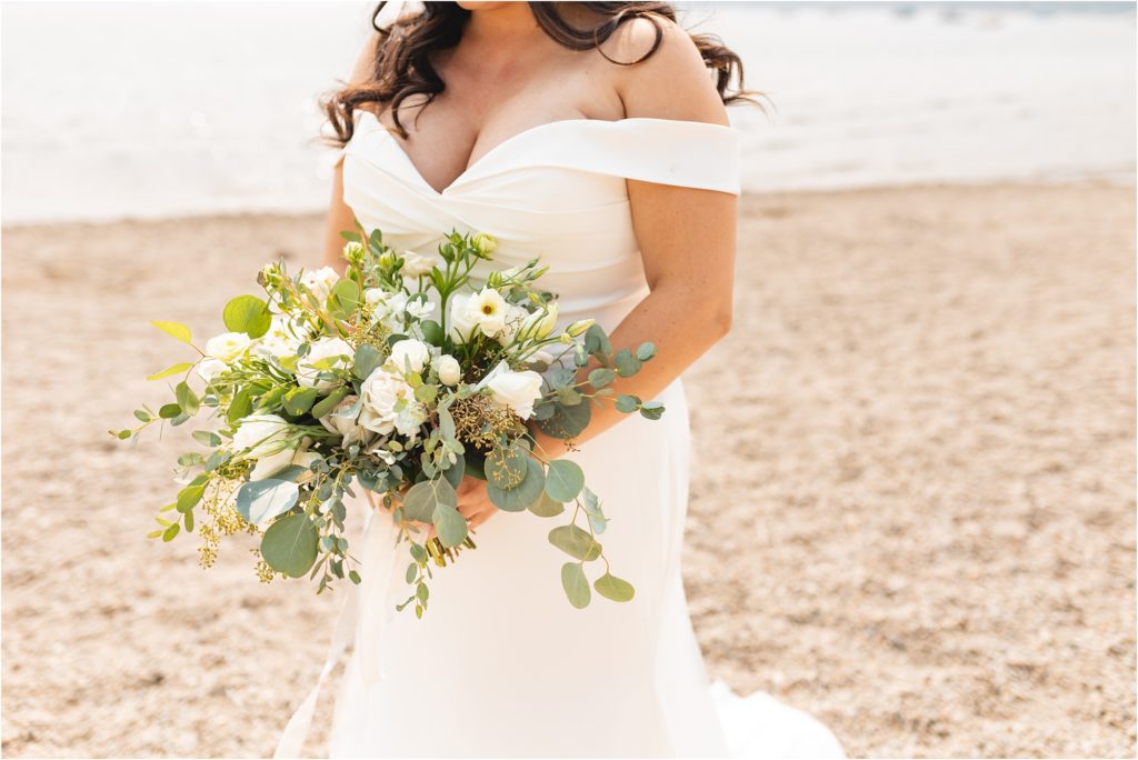 bride holding sage and ivory bouquet on the beach Wedding at Redfish Lake Lodge