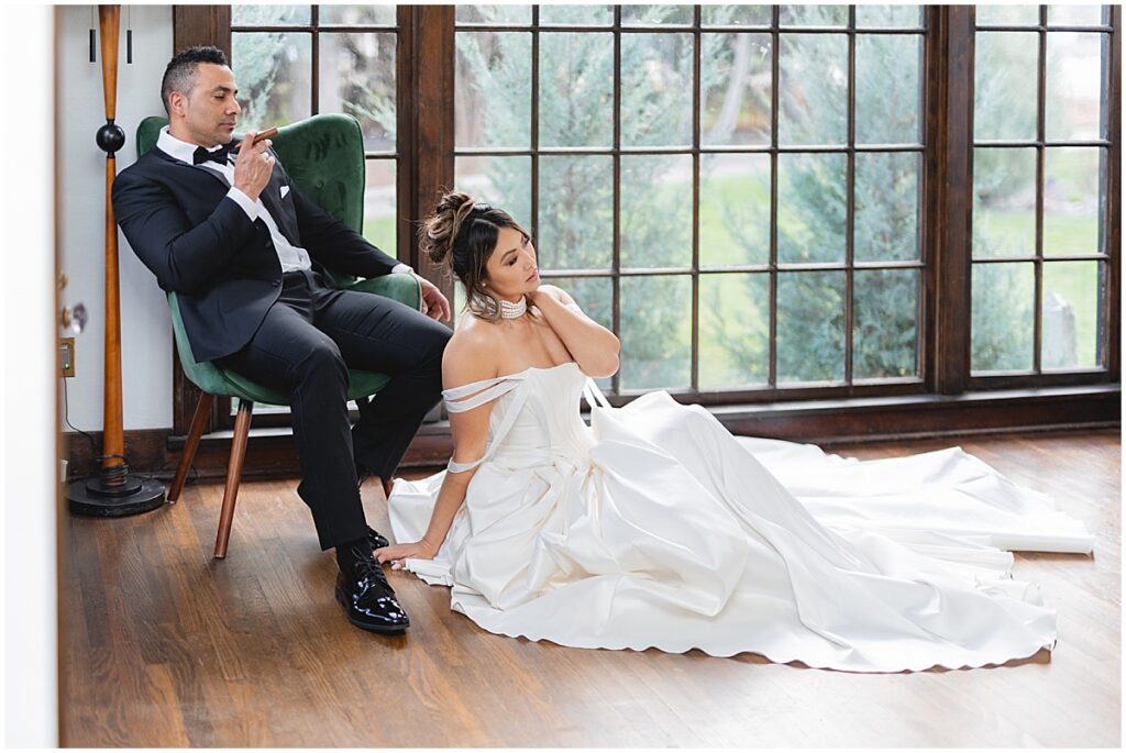 groom sitting in green velvet chair and bride on the floor leaning against his legs