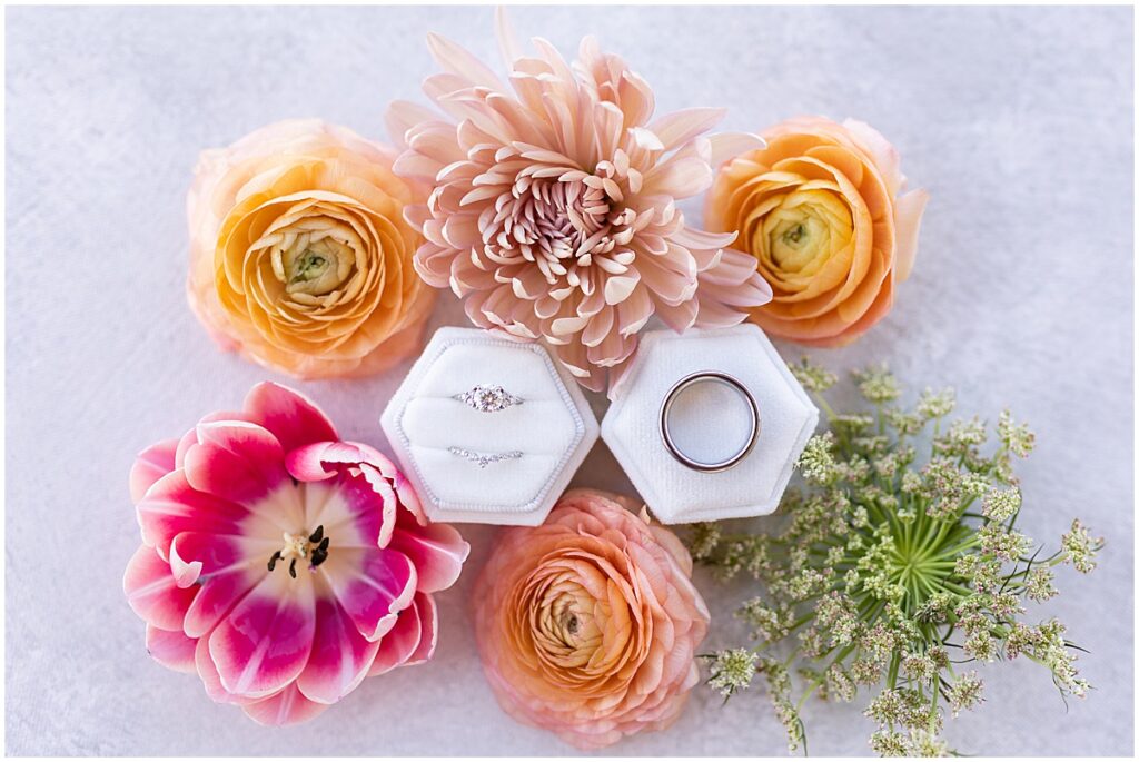 Wedding rings in white velvet ring box surrounded by pink, peach, and orange flowers