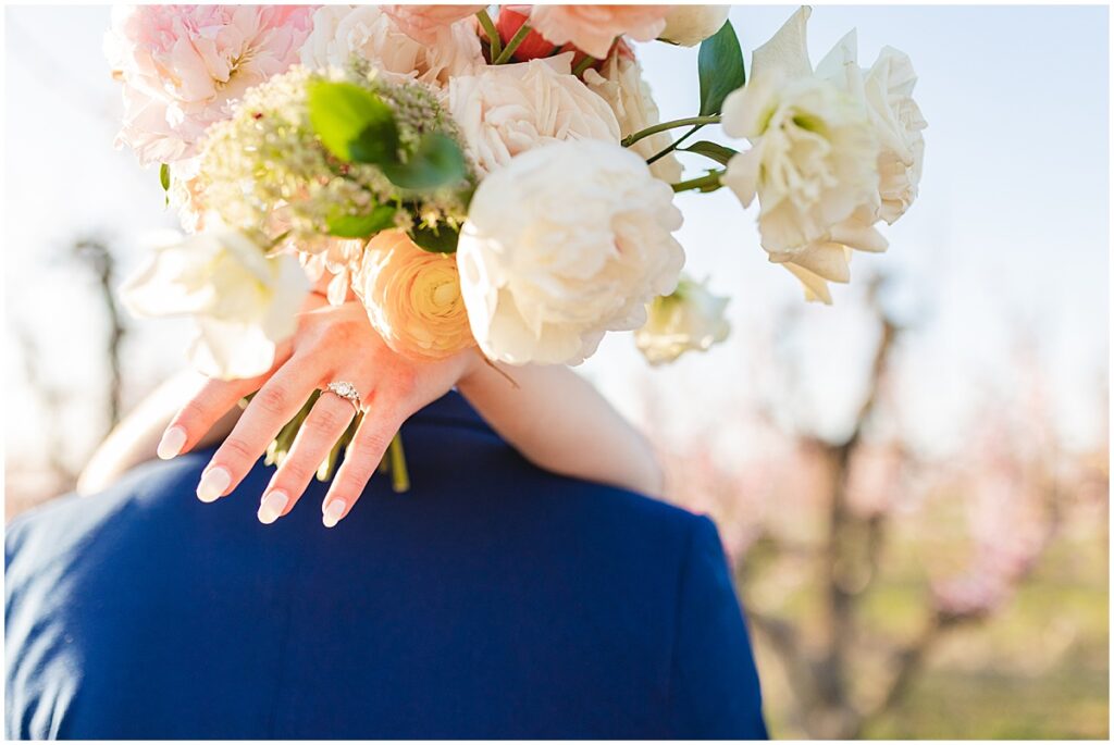 brides hand with wedding ring draped over husbands shoulders holding the bouquet