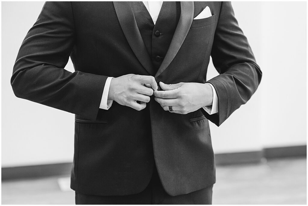 Black and white photo of groom buttoning his tuxedo