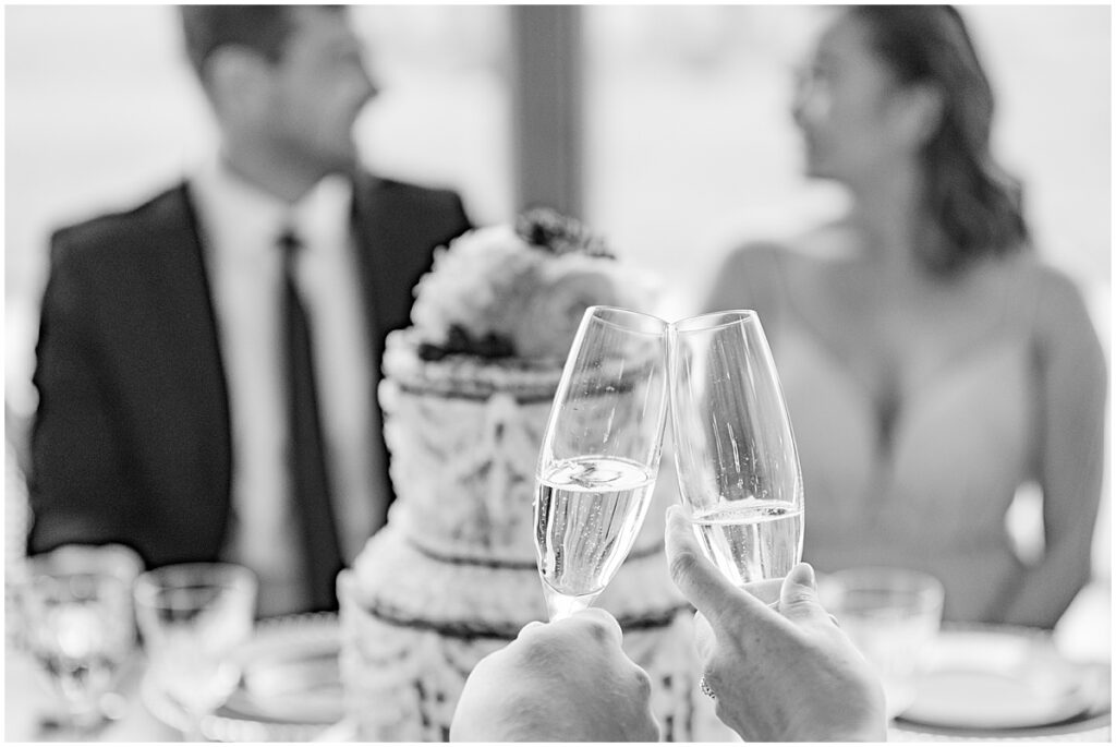 black and white photo of bride and groom toasting with cake in the background