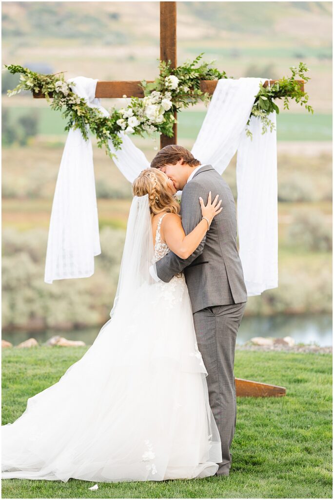 bride and groom first kiss in front of cross at wedding ceremony